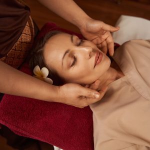 Calm spa client lying in supine position during Thai massage session performed by massotherapist