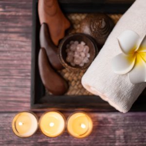 Close up wooden Gun Sha, rolled towel, stone, flower and candle on the tray over wooden background. Facial spa set, wellness well-being lifestyle concept.
